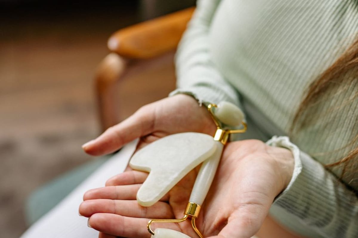 Hands holding a pale jade gua sha stone and a matching facial roller