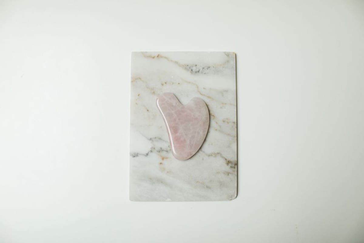 A rose quartz gua sha stone resting on a white marble slab