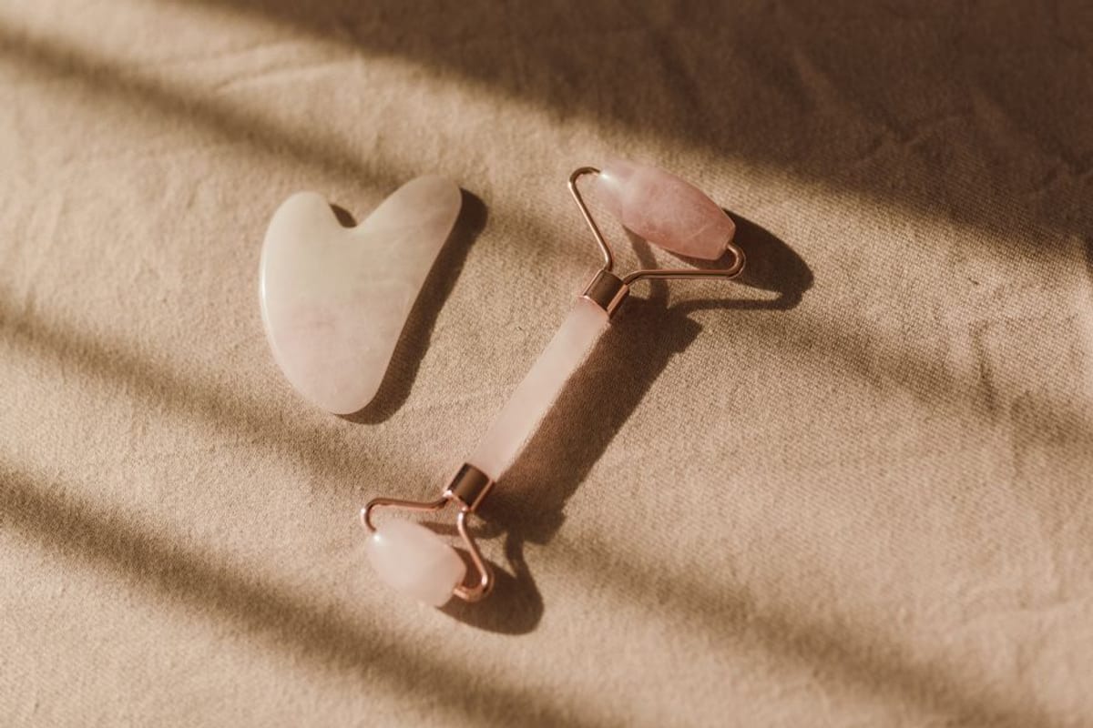 A rose quartz gua sha stone and facial roller resting on beige linen