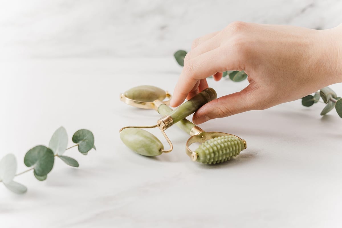 A jade facial roller and gua sha stone on a marble surface