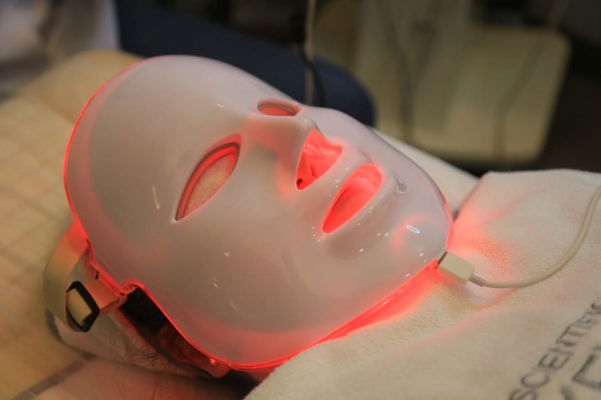 An LED light therapy mask glowing red, face fully covered