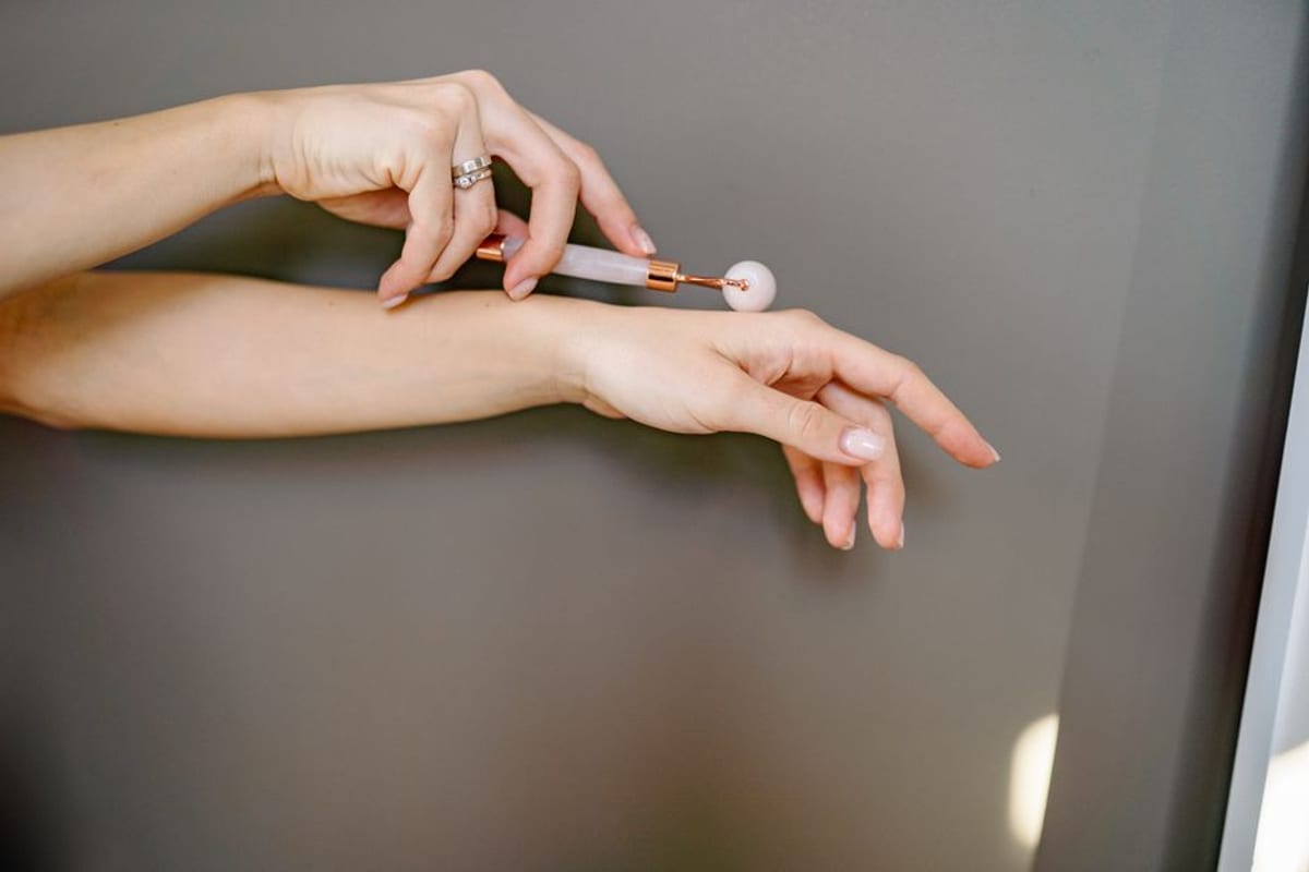 Hands demonstrating a rose quartz roller along the forearm